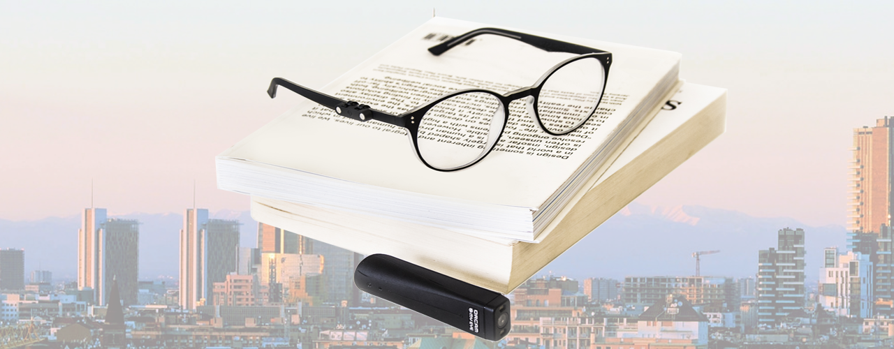 Un paio di occhiali con OrCam MyEye agganciato, appoggiati su due libri aperti